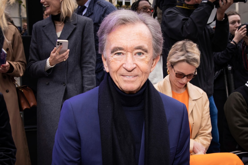 An older man in a jacket and a scarf at a fashion show