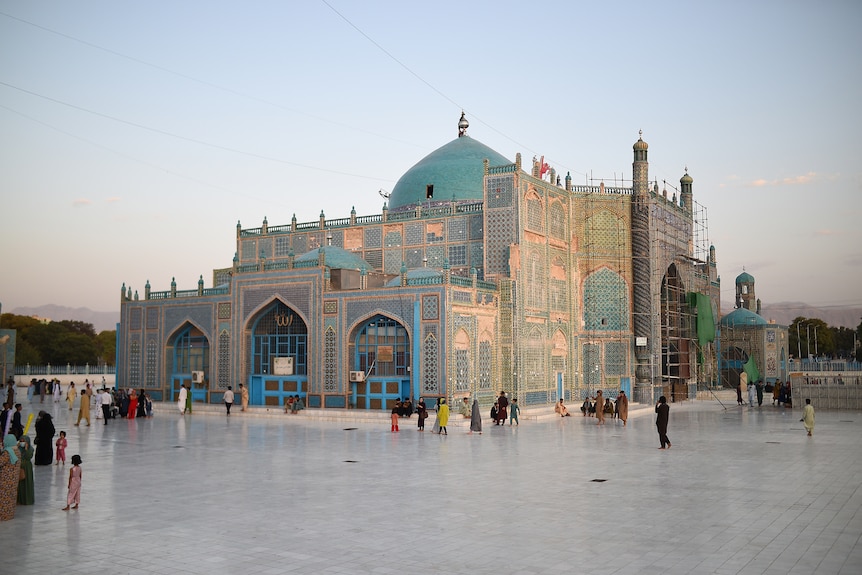 A beautiful golden mosque with blue domes can be seen at the centre of a paved square. 