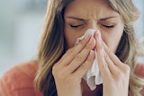 Close-up photo of an unwell woman blowing her nose with a tissue.