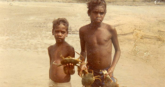 Two Aboriginal boys stand in water holding mud crabs
