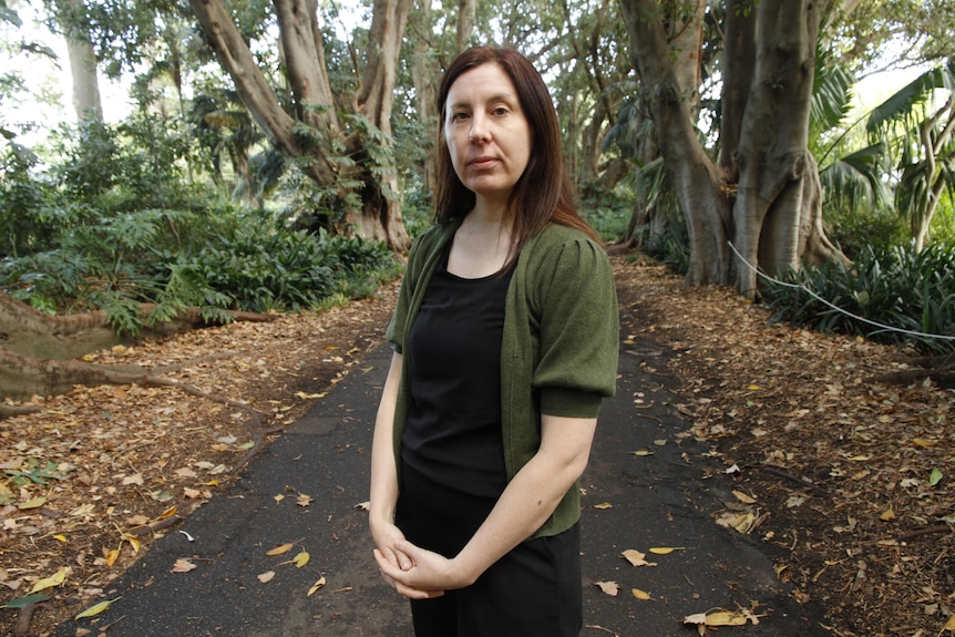 Woman wearing a black top and green cardigan standing in a park.