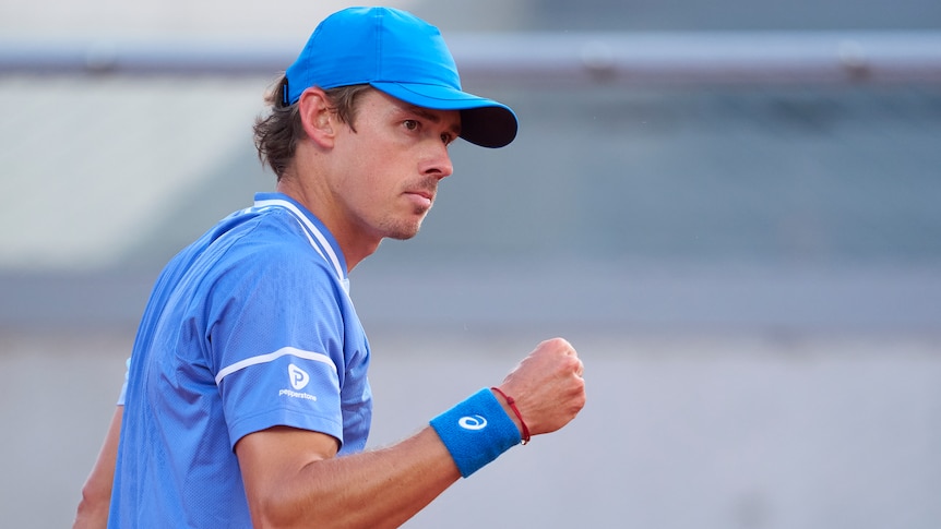 Alex de Minaur, wearing blue tennis gear, clenches his fist after a point at the French Open.