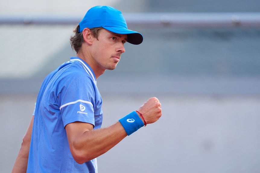 Alex de Minaur, wearing blue tennis gear, clenches his fist after a point at the French Open.