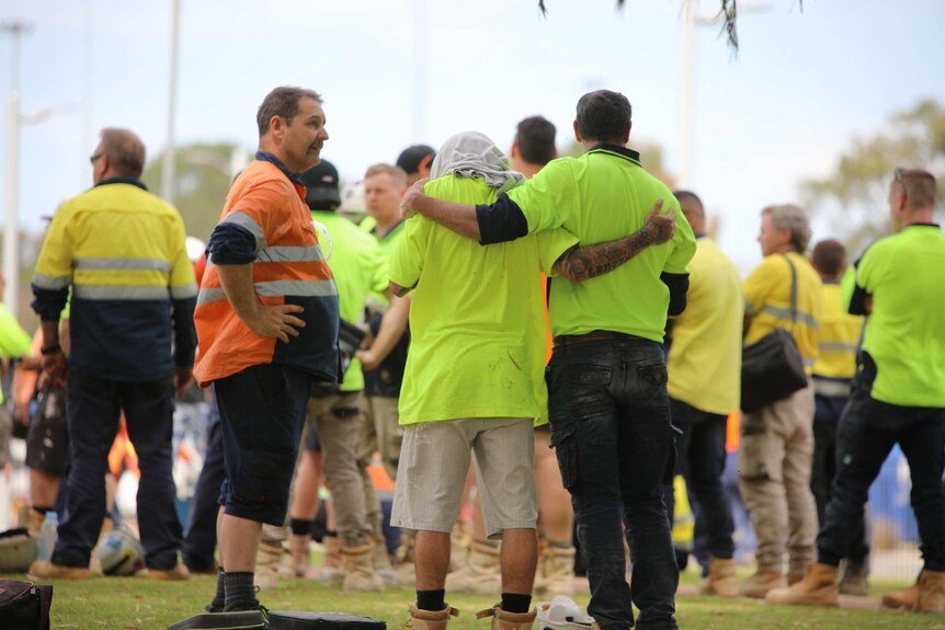 Two workers in hi-vis clothing stand arm in arm at Curtin University with others around them.
