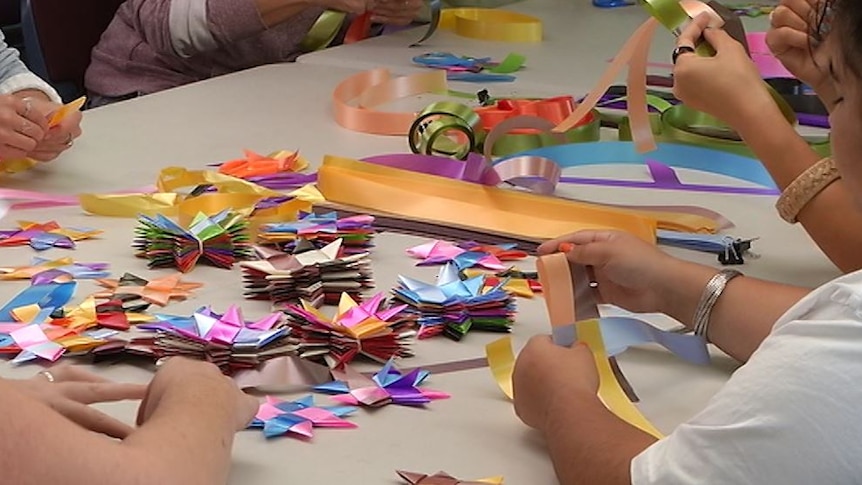 people sit around a table with ribbon and completed folded stars