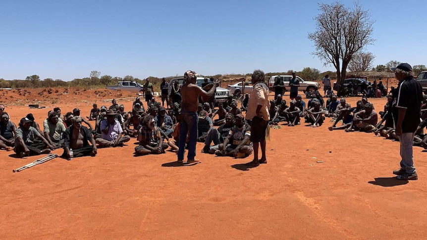 A gathering of people sit on the dirt in Yuendumu.