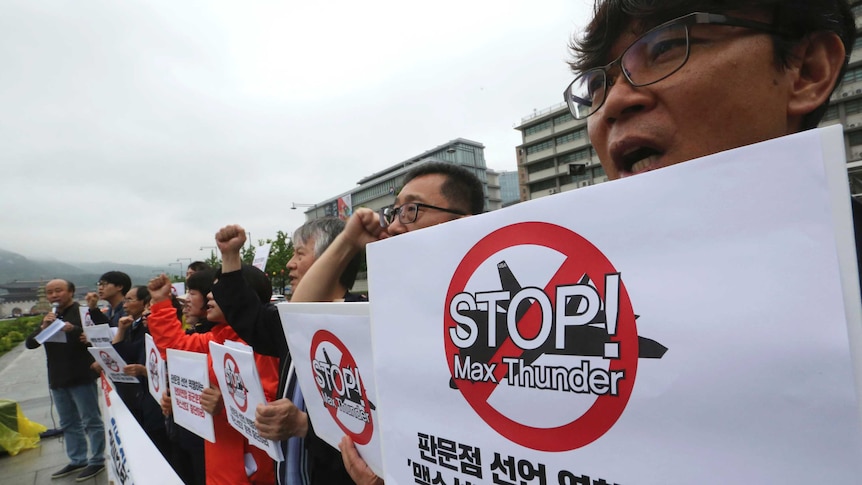 South Korean protestors hold signs saying Stop Max Thunder!