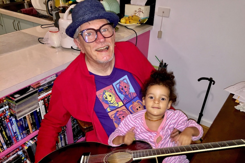 A granddad holding his grandchild with a guitar