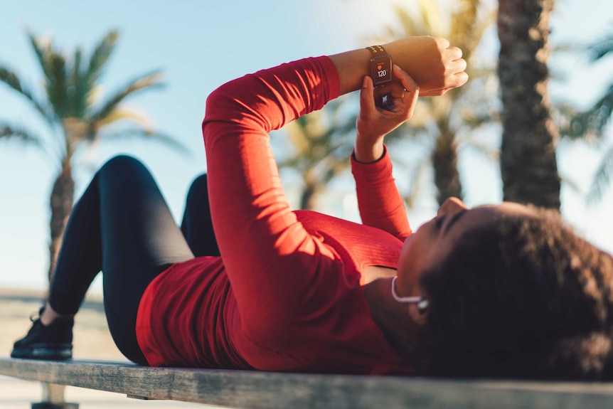 A woman resting on a park bench and tracing her pulse on a smartwatch.