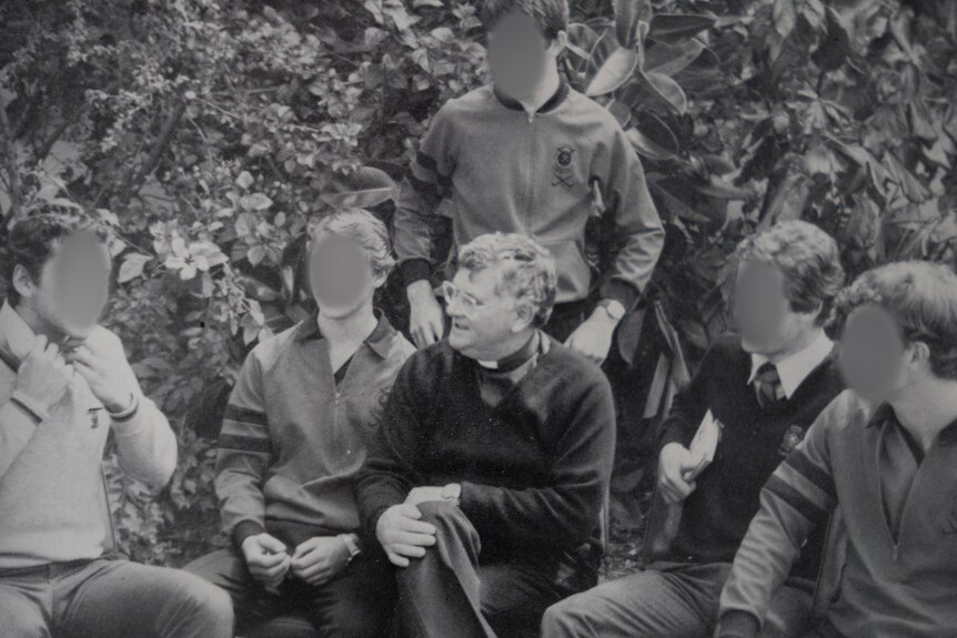 A black and white photo of Daniel McMahon surrounded by students whose faces have been blurred.