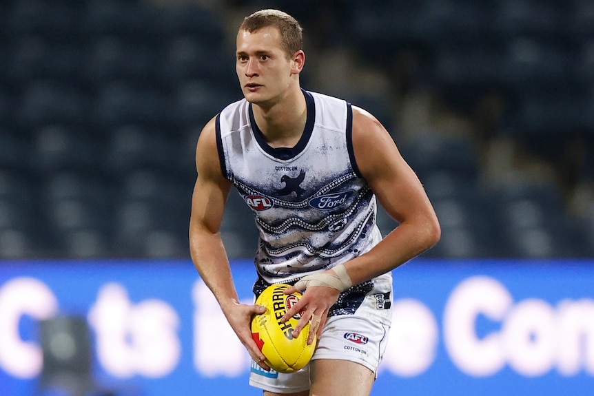 A Geelong AFL player holds the ball as he prepares to kick against GWS during the 2021 season.