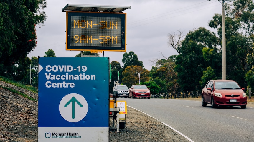 A road sign reads 'MON-SUN 9AM-5PM', beside a COVID-19 Vaccination Centre sign.
