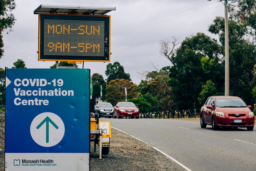 A road sign reads 'MON-SUN 9AM-5PM', beside a COVID-19 Vaccination Centre sign.