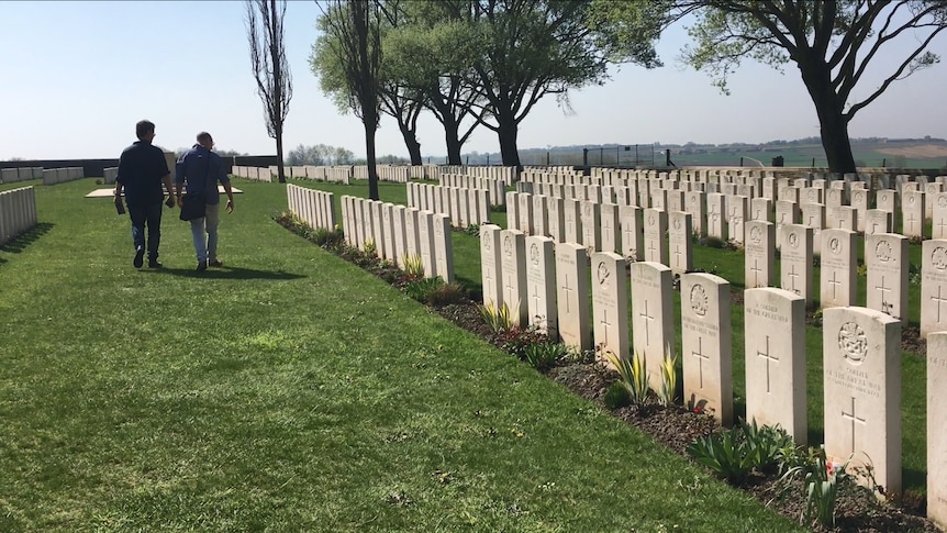 Two men walking alongside white headstones in a war cemetary in France.