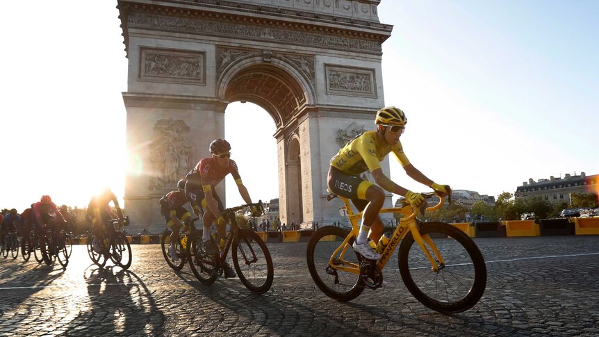 The sun sets behind the Arc de Triomphe with riders in front of it.