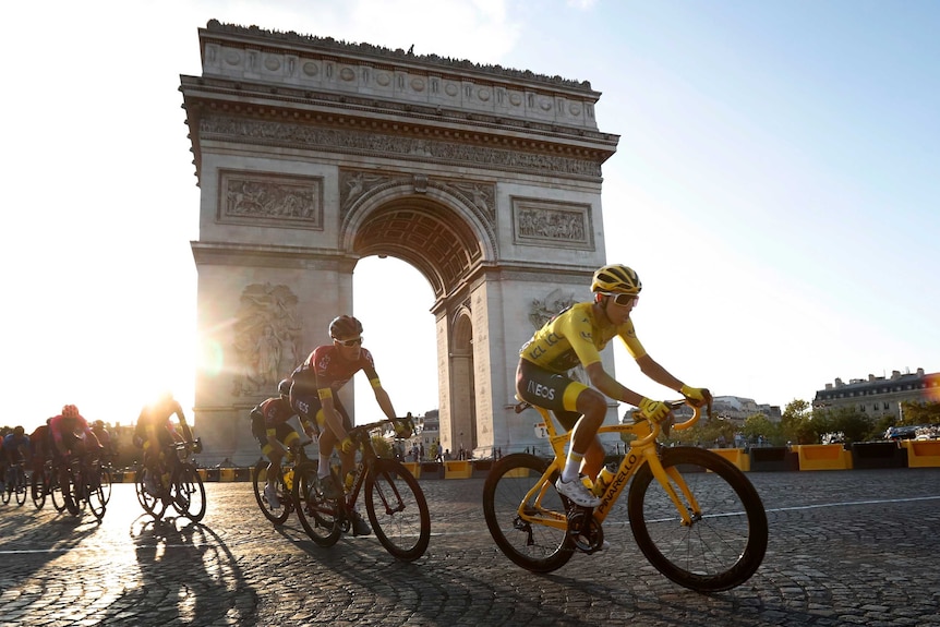The sun sets behind the Arc de Triomphe with riders in front of it.