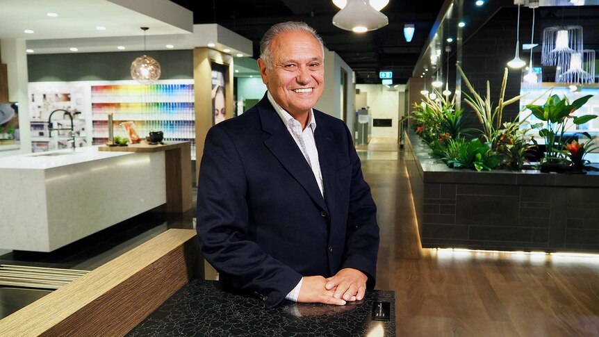 A man in a black suit stands in the middle of a home showroom smiling.