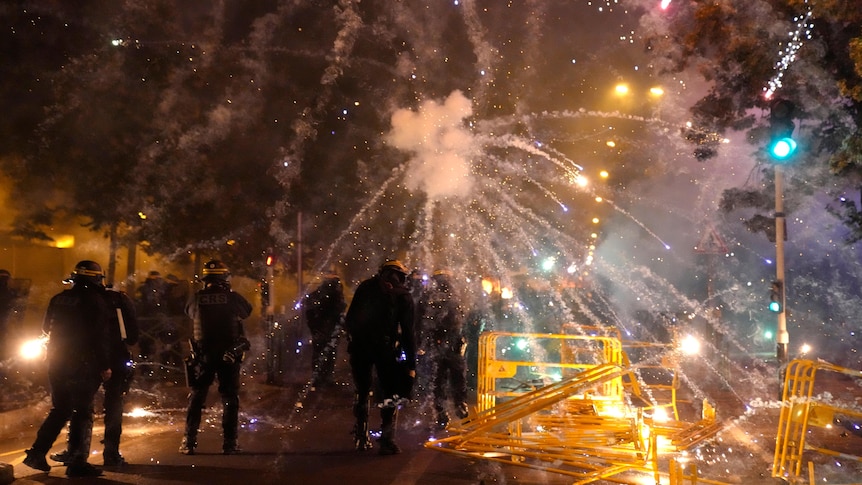 Police in riot gear is pictured as fireworks are going off all around them.