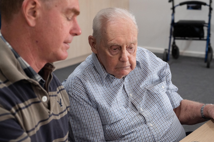 An elderly man sitting listening to younger man.