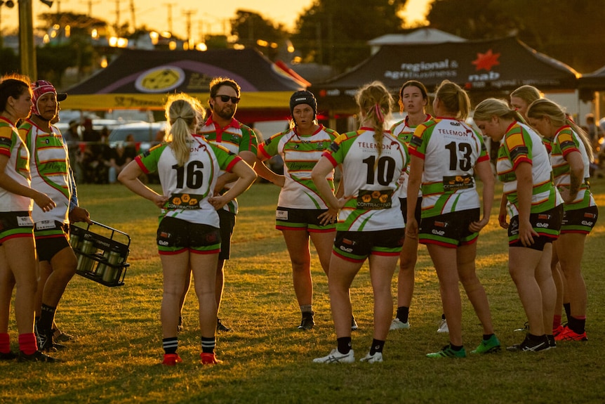 The Hughenden Rams women's team dressed in green and white uniforms stand in a huddle on the field.