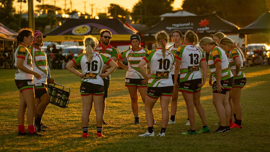 The Hughenden Rams women's team dressed in green and white uniforms stand in a huddle on the field.