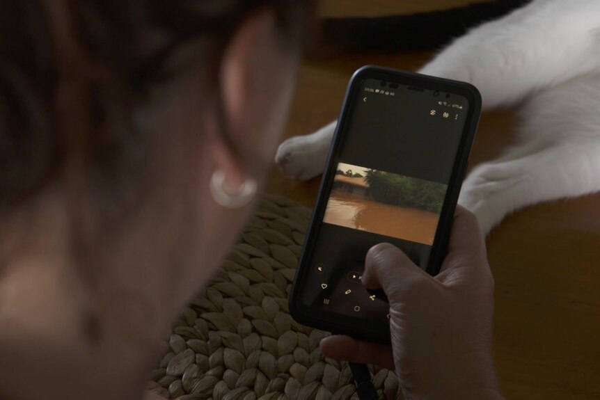 A woman looks at a photo of her flooded house on a phone.