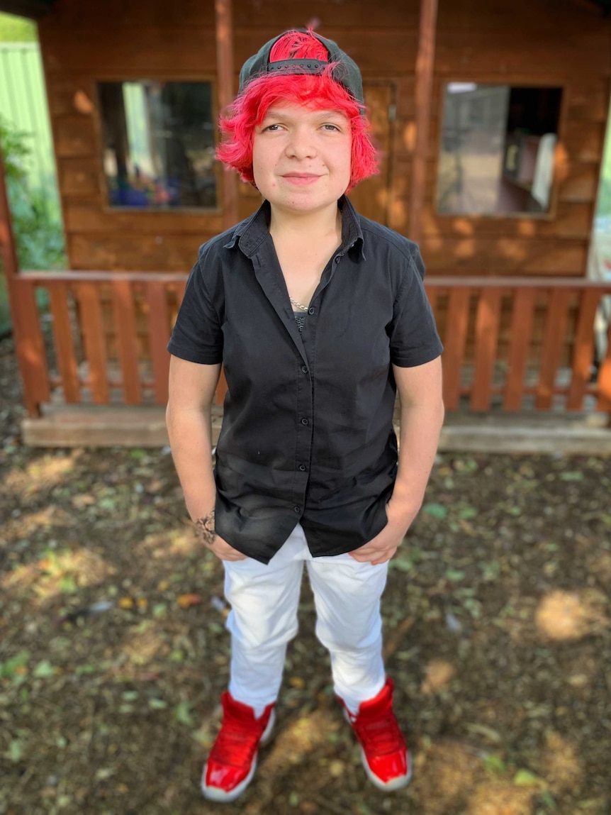 Girl with bright red hair, backwards cap and black shirt smiles at camera.