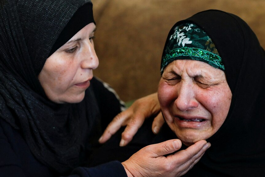 Two women wearing black headscarves comfort one another at a funeral.