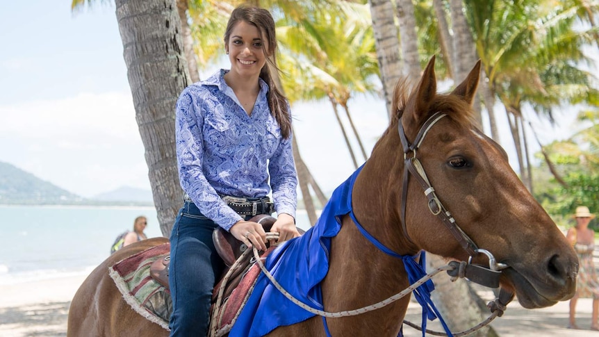 Smiling race winner Simone Pringle wears a purple paisley shirt while sitting in a saddle of her chestnut horse, Chisholm.