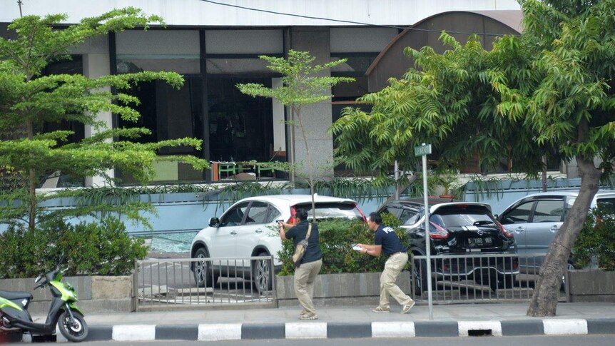 Plain clothes police officers draw handguns outside a Starbucks Coffee towards Jakarta bombing suspects inside.