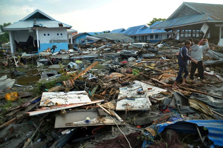 Indonesian men survey the damage as houses lay crushed