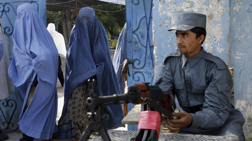 An Afghan policeman keeps watch as women arrive at a polling station