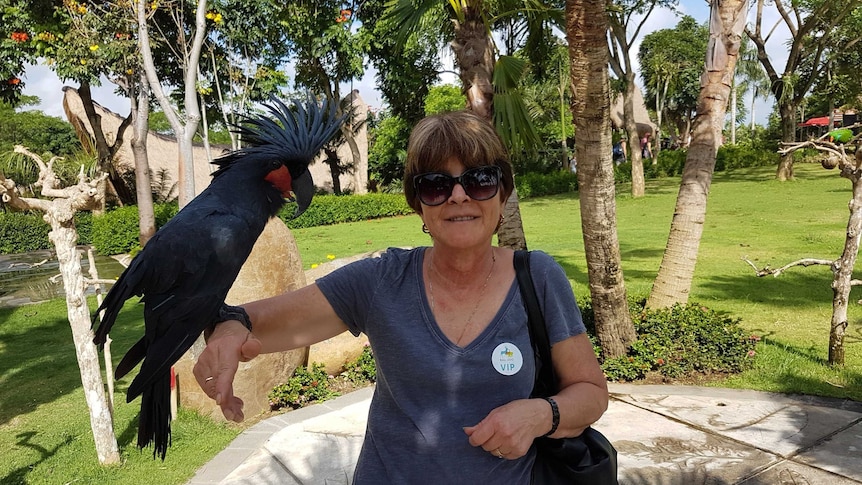 Carolyn Robertson, a woman with short hair, smiles with a large bird on her arm at a park.