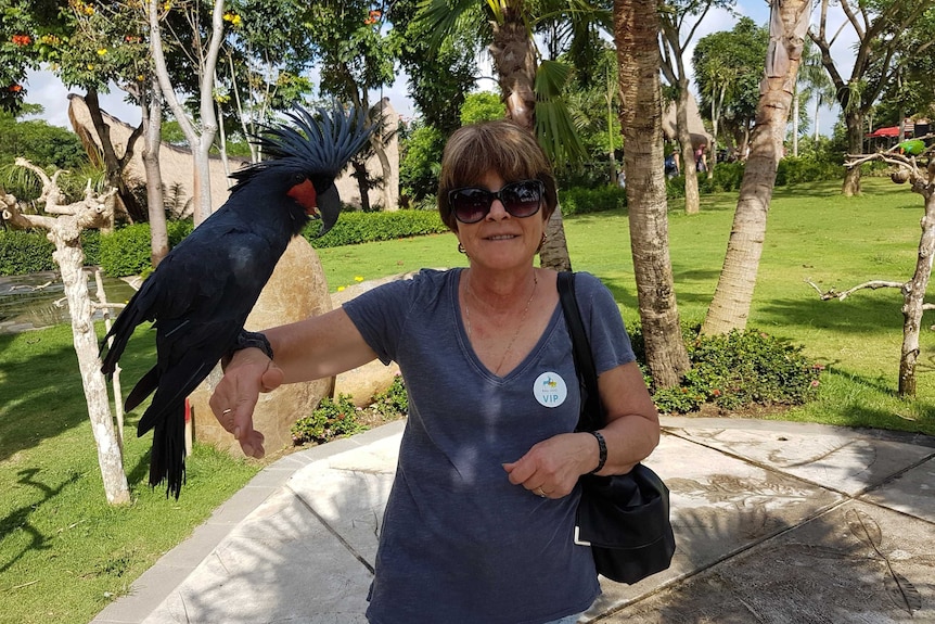 Carolyn Robertson, a woman with short hair, smiles with a large bird on her arm at a park.