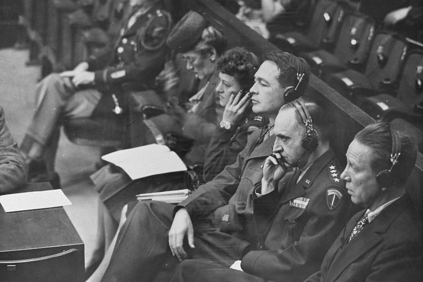 A black and white photo of men and women sitting in a court room wearing headsets.