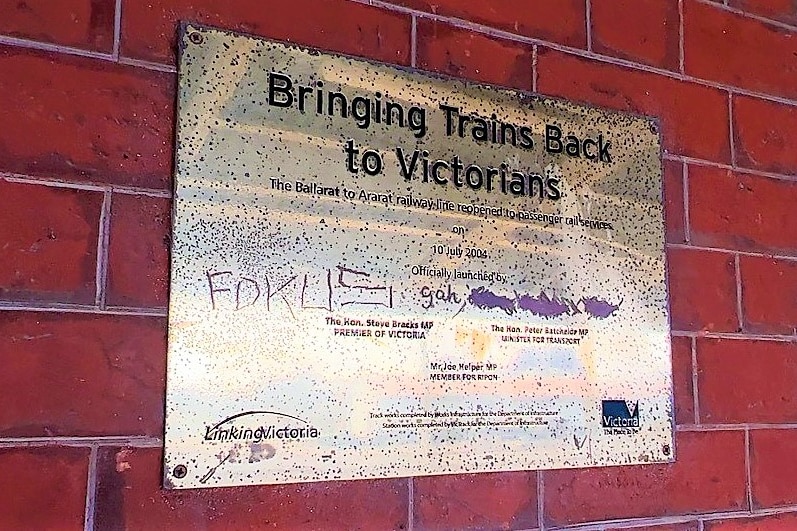 A shiny gold plaque engraved "Bringing trains back to Victorians" mounted on a red brick wall.