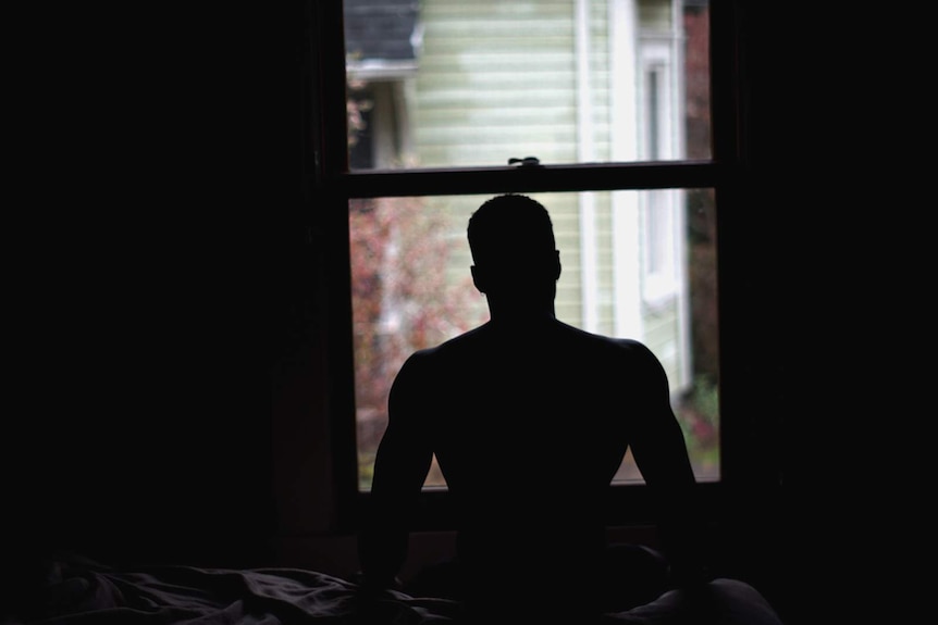 Young man in silhouette on a bed in front of a window