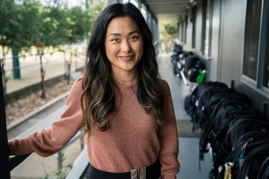 Sarah Woo wearing a pink top and smiling outside a classroom.