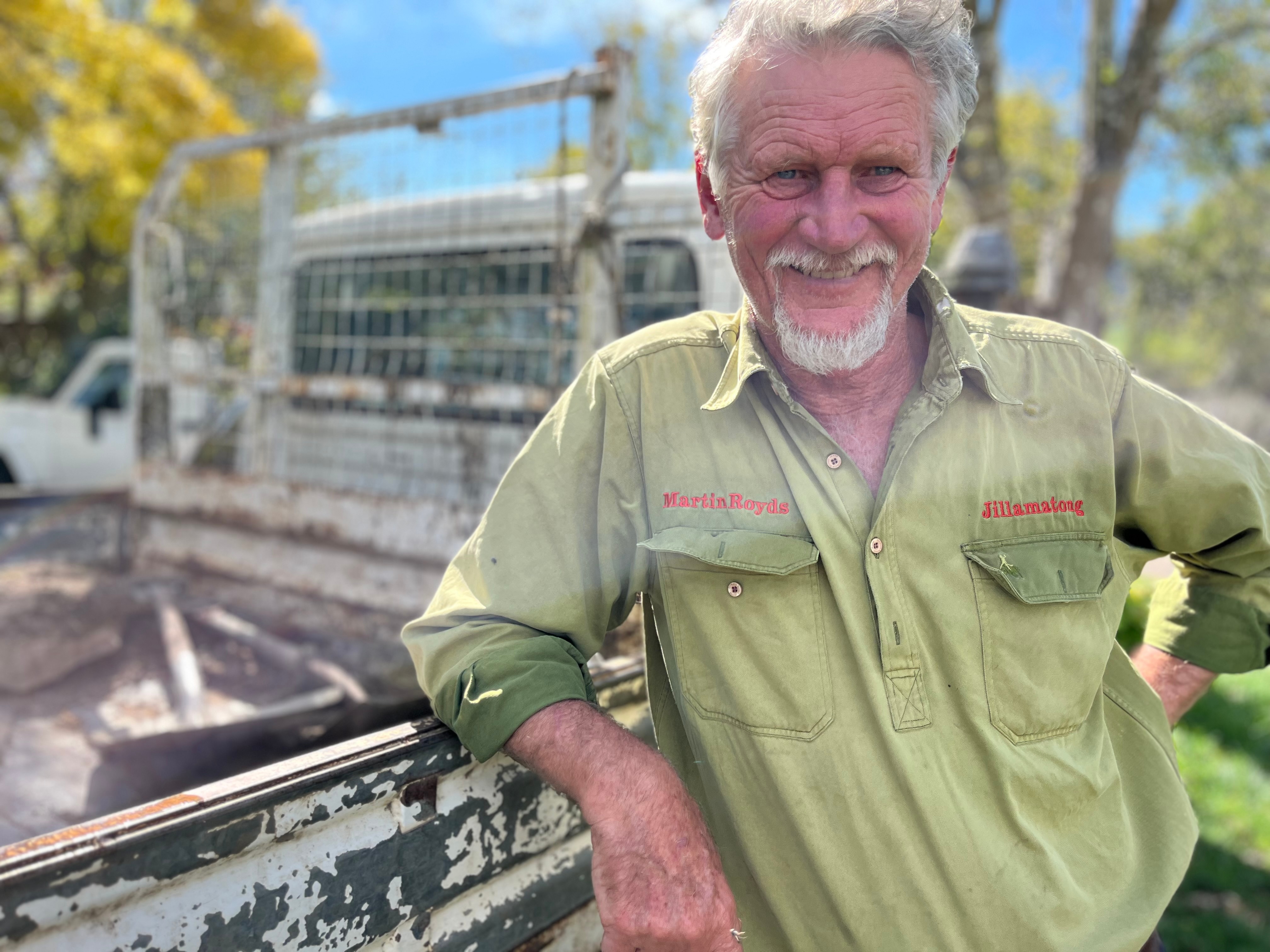 A farmer in a green shirt stands smiling.
