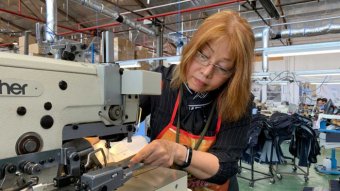 A Vietnamese woman with blonde hair and glasses at a sewing machine.