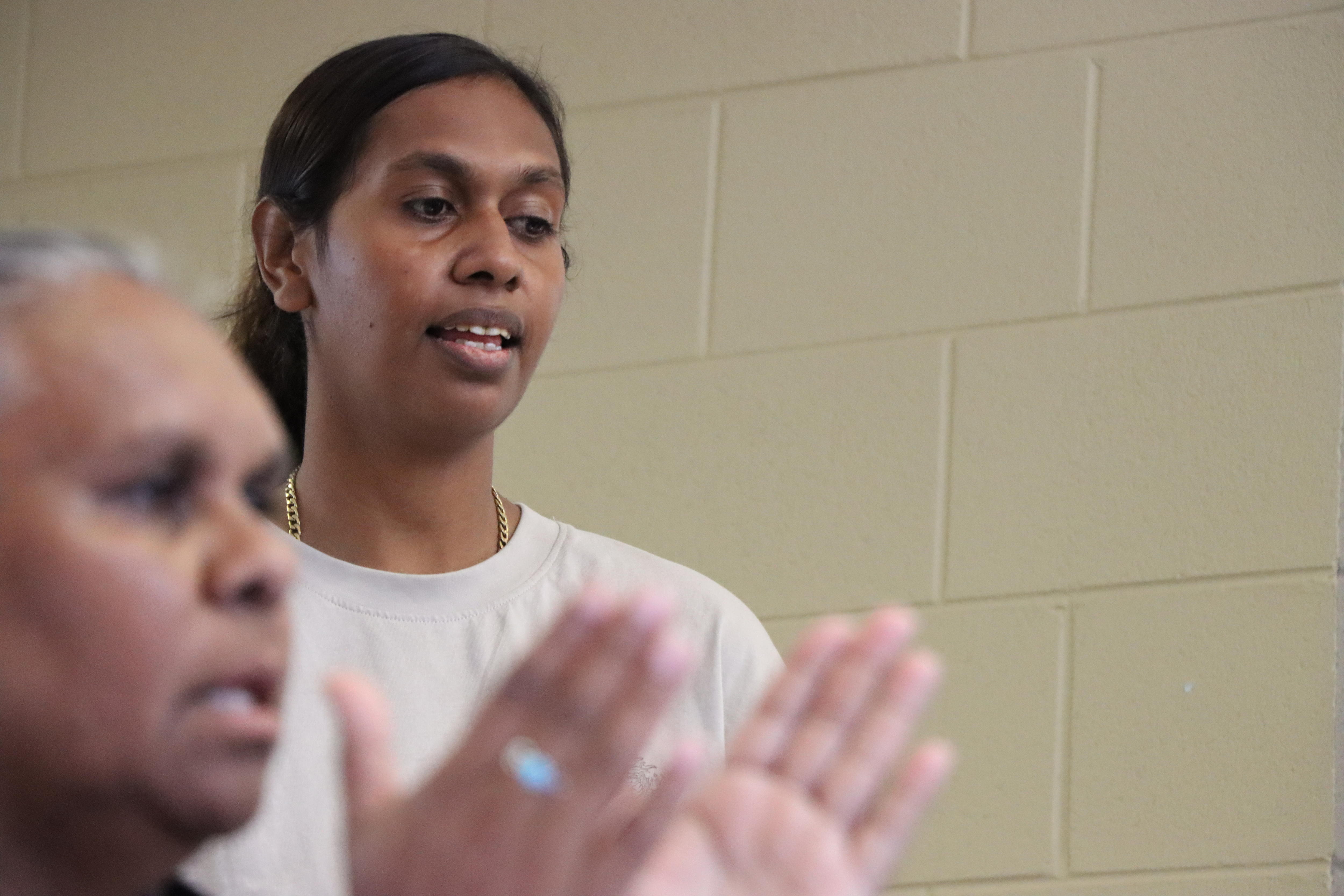 A woman speaks while another person claps in the foreground.