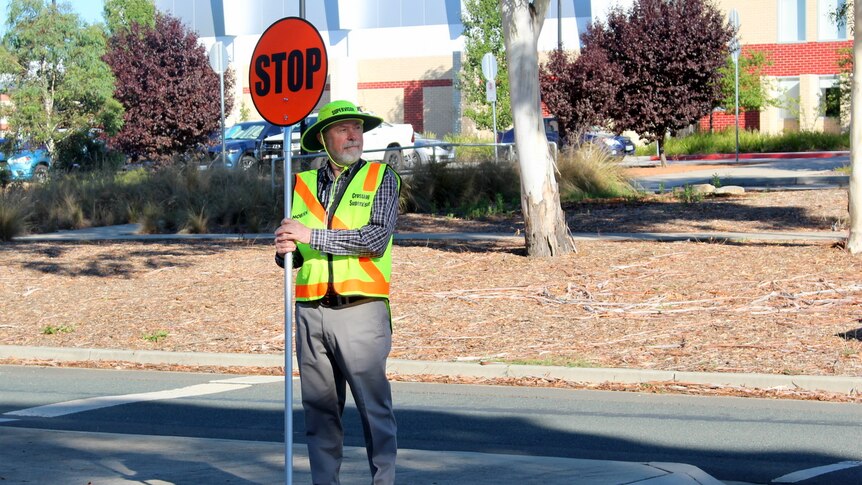 A school crossing supervisor holds a stop sign at a road crossing.