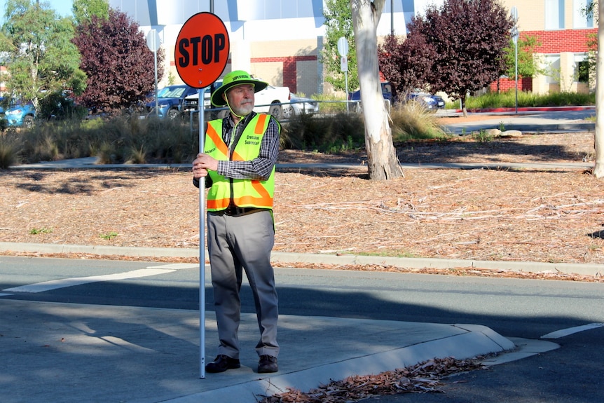 A school crossing supervisor holds a stop sign at a road crossing.