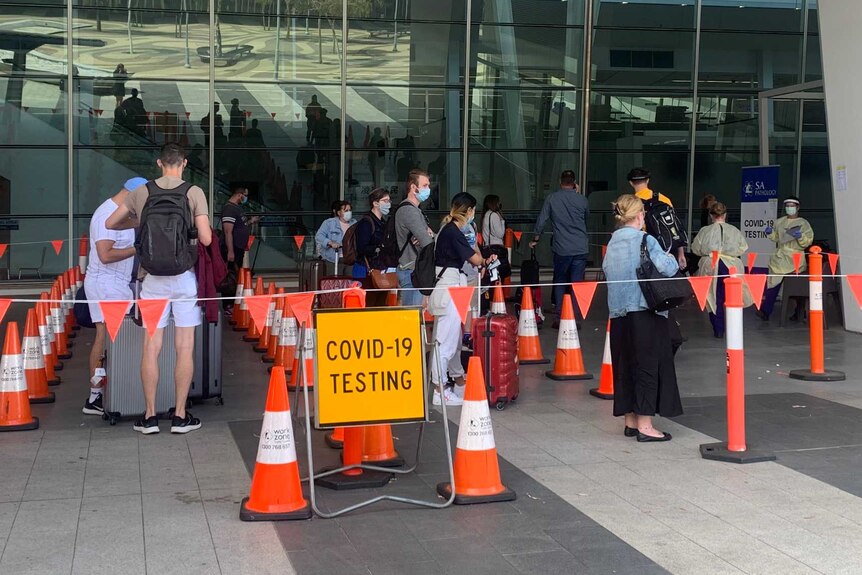 People lining up behind orange flags with a sign saying COVID-19 TESTING