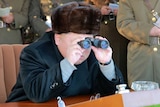 Kim Jong-un looks through binoculars while surrounded by North Korean officials
