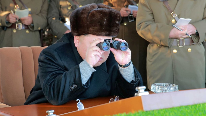 Kim Jon-un looks through binoculars while surrounded by North Korean officials