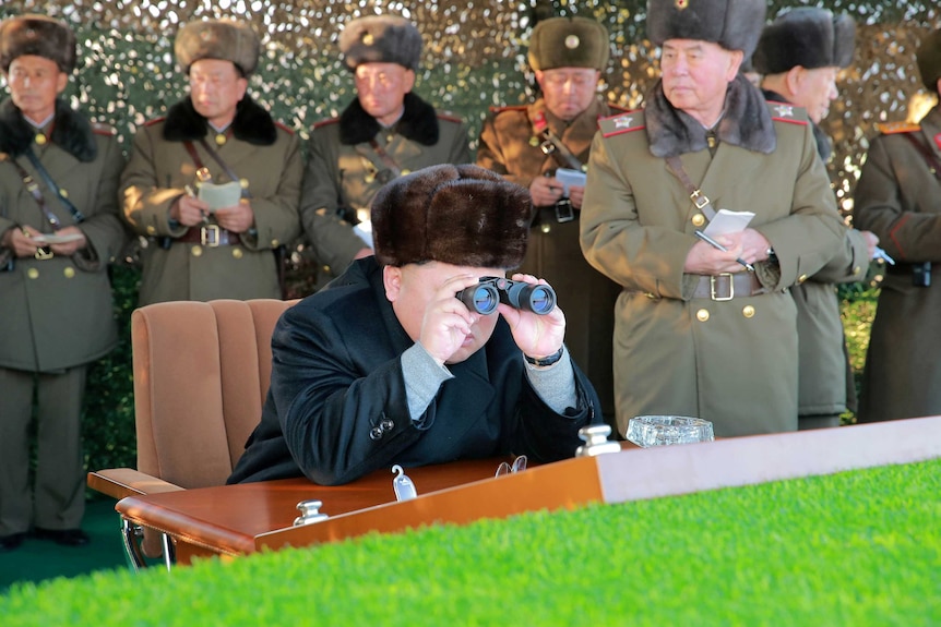 Kim Jon-un looks through binoculars while surrounded by North Korean officials
