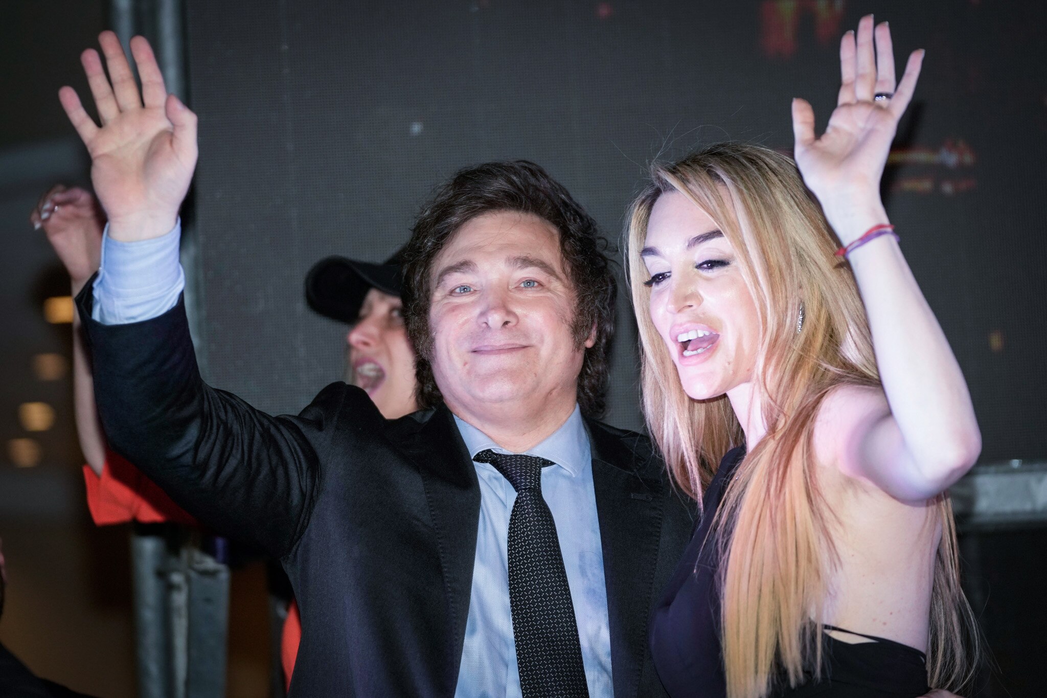 A man and a woman stand on stage waving at a crowd of people.