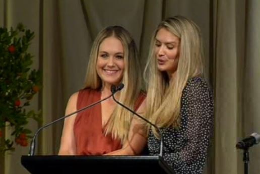 Two blonde women stand at a lectern.