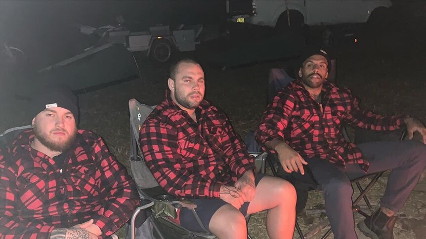 Three guys sit in camping chairs with red and black matching shirts on